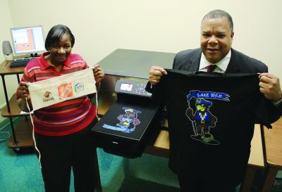 At Charlotte-Mecklenburg Schools’ Graphic Production Center, Debbie Alexander (left), color lab specialist, and Alvin Griffin, director, show off an apron and a shirt printed on the in-plant’s AnaJet mPower mP10 direct-to-garment printer.